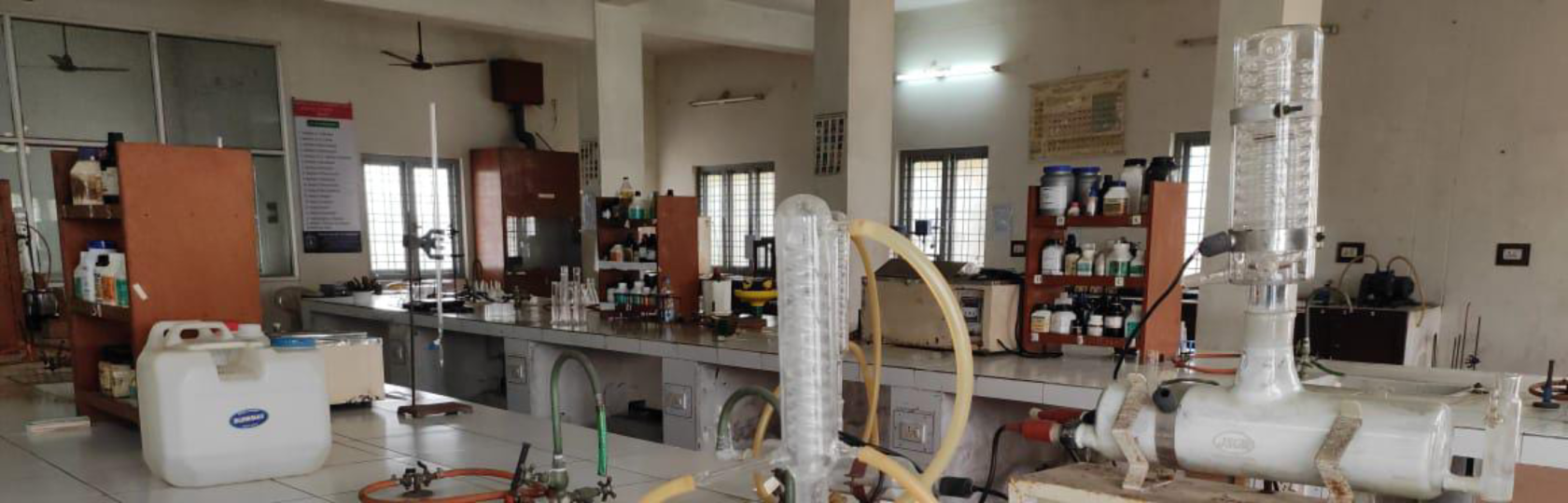 A teaching laboratory at Raghu College of Pharmacy, with glassware and distillation apparatus in use.